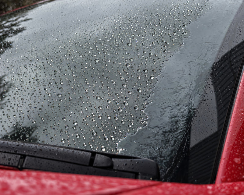 Anti-pluie à l'essai : les gouttes perlent sur le verre traité, un film d'eau reste sur le bord non traité